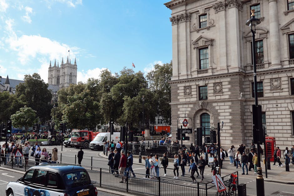 A view of the London Underground station sign indicating Westminster Station, with a black background and white text, mounted on a black metal frame. Behind the sign, the historic Westminster Palace a