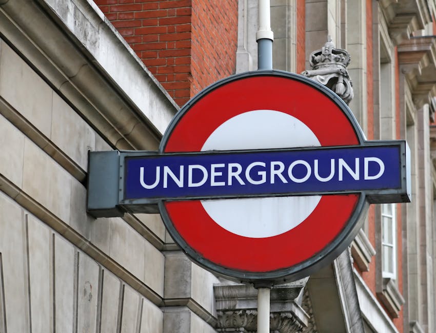 A round London Underground station sign features a red circle with a white center, partially visible behind a rectangular blue sign that reads 'UNDERGROUND' in white capital letters. The sign is mount